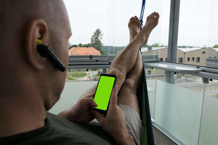 male lying on a hammock with cellphone with green screenの写真素材
