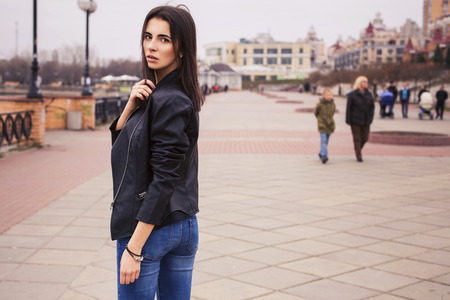 beautiful brunette woman in black leather jacket walking on the european city streetの写真素材