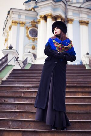 Beautiful brunette russian noblewoman outdoors on autumn day. red lips. black coat and a hat. Ornamental shawl. National traditional outfitの写真素材