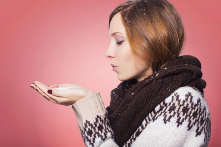Beautiful redhair woman in winter outfit: warm sweater, scarf and hat with snow all over her. Isolated on pink redの写真素材