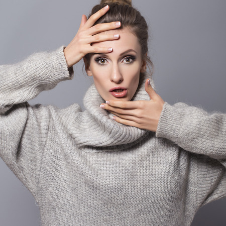 Brunette woman with bun hairstyle and neutral make up posing in grey sweater on a grey backgroundの写真素材