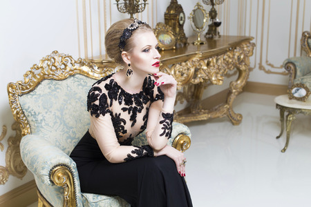 Beautiful blonde royal woman sitting on a retro chair in gorgeous luxury dress. Indoor. Copy Spaceの写真素材