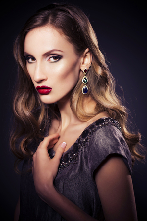 Brunette beautiful luxury woman in dress with clear skin and evening dark make up: green cat eye and brown eyeshadows. Waved hairstyle. Dark backgroundの写真素材