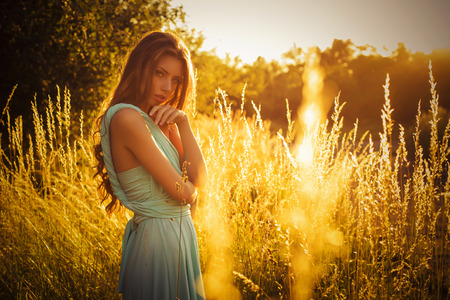 Beautiful blonde with a long curly hair in a long evening dress in motion outdoors in nature in summer sunset. Copy Spaceの写真素材