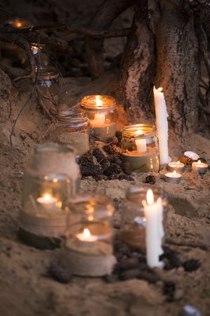 Beautiful decorated romantic place for a date with jars full of candles hunging on tree and standing on a sandの写真素材