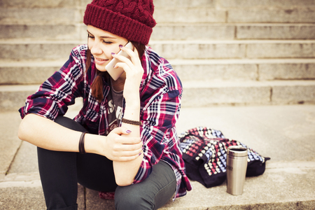 Hipster beautiful woman sitting on the city street, talking on the phone. Generation Z conceptの写真素材