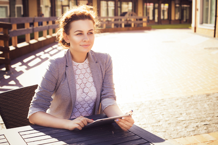 Beautiful brunette woman in grey jacket, dark trousers and white blouse with tablet outdoors. Copy Spaceの写真素材