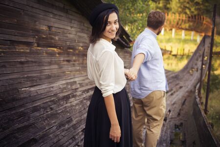 Beautiful hipster couple in love on a date outdoors in park having fun. Bearded redhair man. Brunette woman in black skirt and white blouse and black hat. Follow me. copy spaceの写真素材