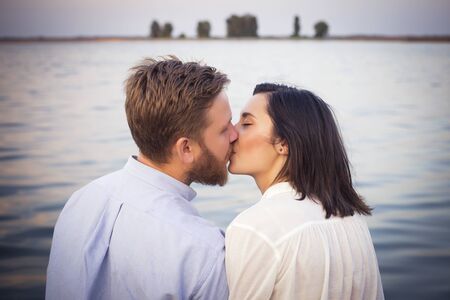 Beautiful hipster couple in love on a date outdoors in park having fun. Bearded redhair man. Brunette woman in black skirt and white blouse. Near river seaの写真素材