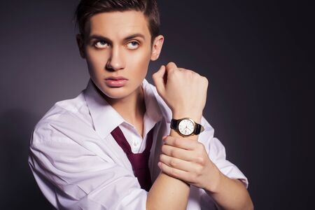 Young handsome men in suit shirt and red tie wear watches looking up. dark background. indoors. copy spaceの写真素材