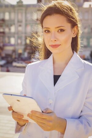 Beautiful brunette business woman in white suit working on a tablet in her hands outdoors. copy spaceの写真素材
