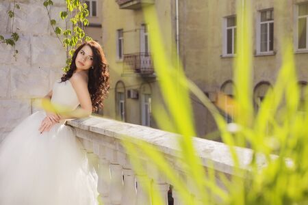 Beautiful brunette woman bride in a garden park in white wedding dress, curly hairstyle and a smile. warm weather, outdoors. copy spaceの写真素材