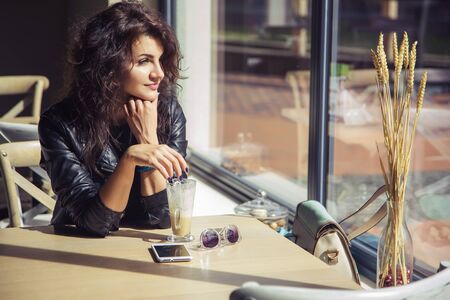 Brunette beautiful stylish caucasian woman in casual outfit on a walk on european city street sitting at the cafe waiting. copy spaceの写真素材