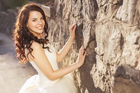 Beautiful brunette woman bride in a garden park in white wedding dress, curly hairstyle and a smile. warm weather, outdoors. copy spaceの写真素材