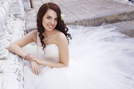 Beautiful brunette woman bride in a garden park in white wedding dress, curly hairstyle and a smile. warm weather, outdoors. copy spaceの写真素材