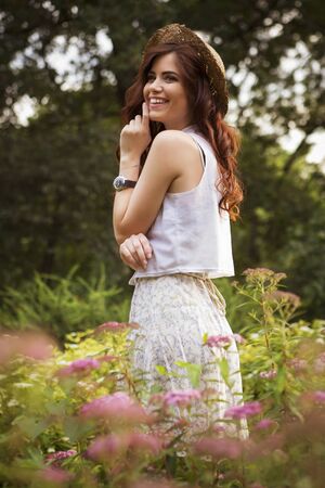 Young beautiful caucasian white brunette woman with curly hairstyle and make up, in a summer outfit: dress and a hat in park. outdoorsの写真素材