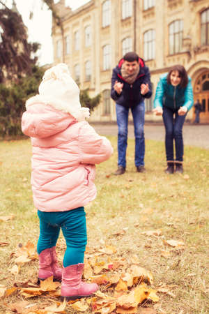Happy loving family(mother, father and little daughter kid) outdoors walking having fun on a park in autumn season. Fallen yellow leaves on a background. Cold weatherの写真素材
