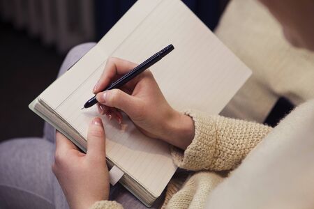 Woman sitting on a couch with a notepad in her hands, working. Writing using pen. Soft light,...