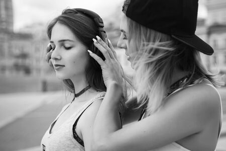Two young beautiful blonde hipster girls on summer day having fun in european city listening music in headphones. Copy spaceの写真素材