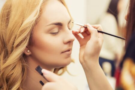 Brunette make up artist woman applying make up for a blonde bride in her wedding day, for a dateの写真素材