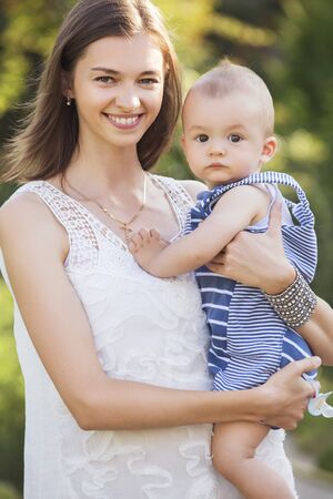 Happy smiling family of slim fit beautiful brunette mother and cute little infant baby in a green...
