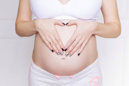Pregnant caucasian white woman standing in white bra and shorts, holding her belly. copy spaceの写真素材