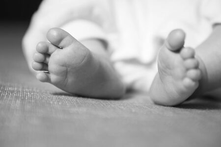 Little infant baby boy sleeping laying, feets up, in focus. Neutral black background, black and...
