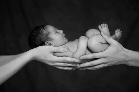 Little infant baby boy sleeping laying on mothers and fathers arms. Neutral black background, black and white picture. Happy familyの写真素材