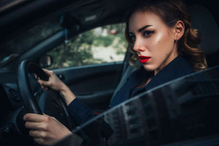 Beautiful brunette spy agent (killer or police) woman in leather jacket and jeans with a gun in her hand driving a car after someone, to catch him.の写真素材