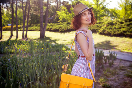Beautiful red haired woman with fresh flawless skin and curly hairstyle in dress and a hat, smiling...
