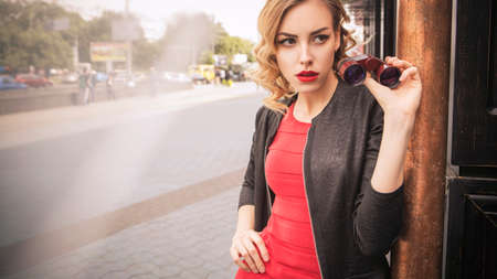 Beautiful brunette spy agent (killer or police) woman in leather jacket and red luxury dress with a...