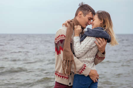 Happy thoughtful couple standing on a rock beach near sea hugging each other in cold foggy cloudy...