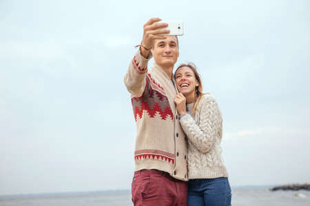 Happy thoughtful couple standing on a rock beach near sea hugging each other in cold foggy cloudy...