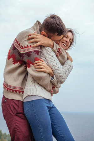 Happy thoughtful couple standing on a cliff near sea hugging each other in cold foggy cloudy autumn weather. Copy spaceの写真素材