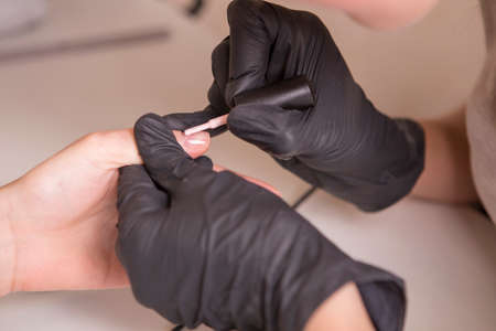 Nail master in rubber gloves apply gel polish shellac on a woman hand finger nail. Healthcare beauty cosmetic spa procedure in a salonの写真素材