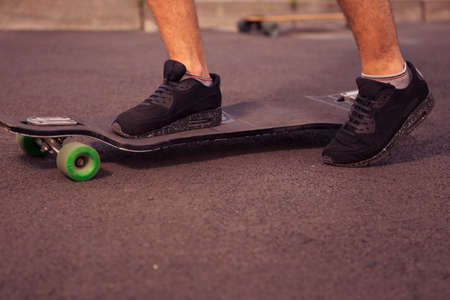 Man feet standing on a longboard on the road, skate in park in summer. Sunset sun. Active leisure...