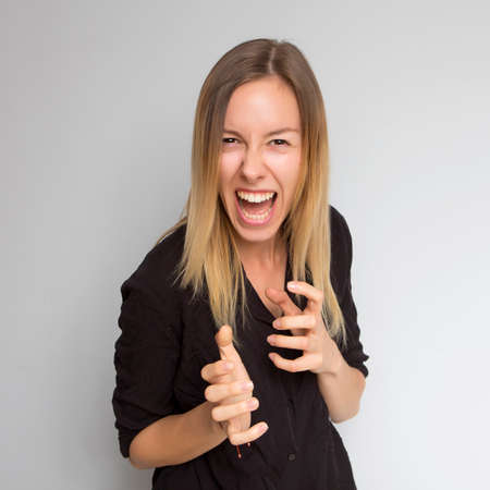 Beautiful brunette caucasian woman in dark black blouse with bright emotions standing on a neutral grey background. Her hands make a gesture. She smiling happilyの写真素材