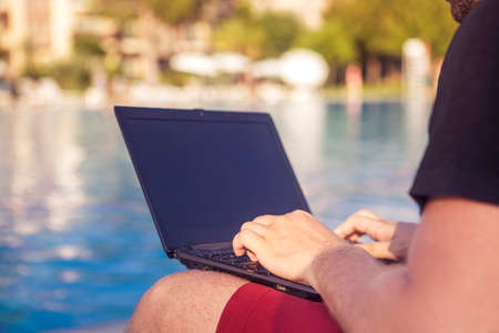 Businessman working typing on a laptop computer on his vacation trip in tropical country, sitting...