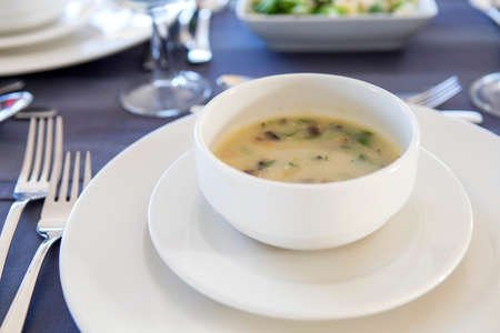 Delicious seafood meal soup with fish and vegetables on a plate in the restaurant. Spoons, forks and knives on the table, all prepared for celebration evening. Dim sunset light, outdoorsの写真素材