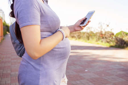 Beautiful brunette caucasian pregnant woman on summer walk outdoors, holding her belly in a soft,...