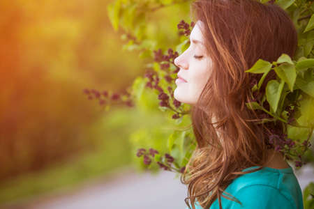 Cute ordinary caucasian brunette woman in casual outfit walking at the nature park, posing sensually in flowers. Cold spring (autumn) weather, warm dress on a girl. Sunset. Copy spaceの写真素材