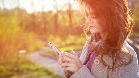 Cute ordinary caucasian brunette woman in casual outfit walking at the nature park. Cold spring (autumn) weather, warm coat on a girl. Sunset. Copy spaceの写真素材