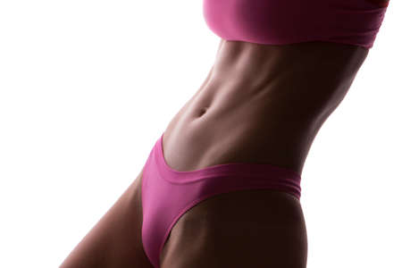 Close up of a beautiful caucasian young woman fit athletic body in sportswear pumping up abdominal muscles. Neutral white isolated backgroundの写真素材