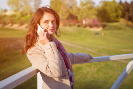 Cute ordinary caucasian brunette woman in casual outfit walking at the nature park, posing sensually in flowers. Cold spring (autumn) weather, warm dress on a girl. Sunset. Copy spaceの写真素材