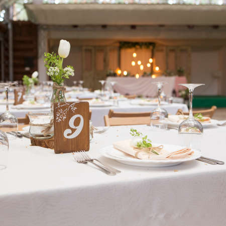Simple but luxury rich table setting for a wedding celebration in nice cozy restaurant. Wineglasses, plates and bouquet of summer seasonal flowers on a table. Sunlight from a window. Copy spaceの写真素材
