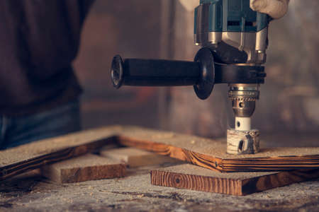 Man drill holes in wooden plank with lighting and cords. Man at handmade diy workの写真素材
