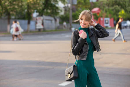Beautiful rich luxury looking blonde caucasian business woman in casual green outfit standing on a european streets, holding coffee and purse. Daylight, outdoors.の写真素材