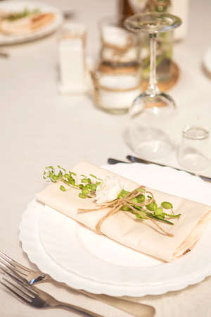 Simple but luxury rich table setting for a wedding celebration in nice cozy restaurant. Wineglasses, plates and bouquet of summer seasonal flowers on a table. Sunlight from a window. Copy spaceの写真素材