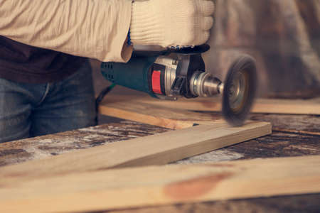 Carpenter using electric grinder to cut a wooden board.
