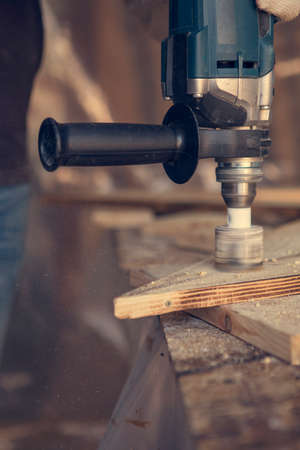 Man drill holes in wooden plank with lighting and cords. Man at handmade diy workの写真素材